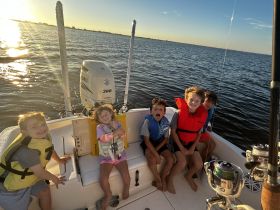 A joyful group of children wearing life jackets enjoys a sunset boat ride, capturing the essence of fun and adventure on the water.