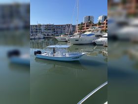 A picturesque view of the boat 'La Otra' docked in a marina, surrounded by luxury yachts and vibrant buildings, perfect for fishing or leisure outings.