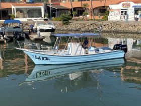 A fishing boat named 'LA OTRA' is docked in a marina, showcasing its sleek design and reflecting beautifully on the water.