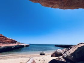 A serene view of a small boat anchored on a sandy beach, framed by stunning red rock formations and clear blue skies — perfect for a peaceful getaway.