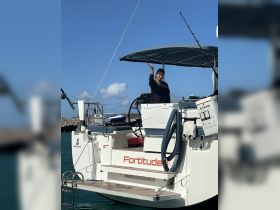 A woman waves from the helm of the Beneteau yacht 'Fortitude,' showcasing the inviting atmosphere of a day on the water.
