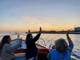 A joyful group waves at sunset from their boat, capturing a memorable moment on the water — perfect for family outings or sunset cruises.