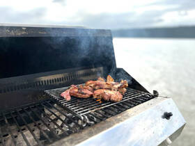 A close-up of grilled meats sizzling on a barbecue aboard a boat, perfect for outdoor dining experiences on the water.