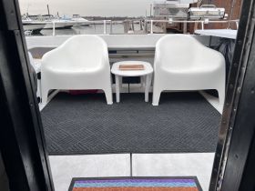 A cozy interior view of a boat featuring white seating and a small table, perfect for relaxing while enjoying the water.