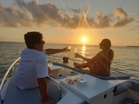 A couple enjoys a romantic toast with cocktails on the deck of a boat at sunset, creating the perfect atmosphere for a memorable sunset cruise.