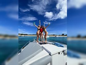 Three friends celebrate on the bow of a boat, enjoying a sunny day by the beach — perfect for fun-filled outings and memorable gatherings on the water.