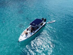 A lively group enjoys a day on the water aboard a boat, surrounded by stunning turquoise waters, with a paddleboard ready for fun.
