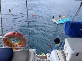 A lively scene of guests enjoying snorkeling and floating on a raft in clear waters, showcasing the fun and adventure of a day on the boat.