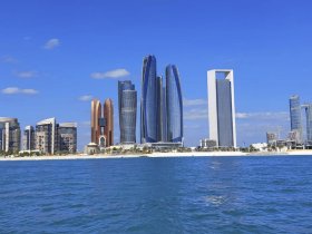 A stunning view of the Abu Dhabi skyline from the water, showcasing modern architecture against a clear blue sky — perfect for city tours and sightseeing.