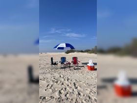 A serene beach setup featuring colorful chairs, a cooler, and an umbrella, perfect for a relaxing day by the water.