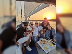 A joyful family gathers on a sailboat at sunset, enjoying drinks and snacks together — a perfect moment for celebration and bonding on the water.