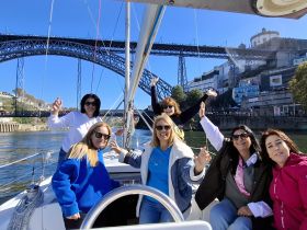 A joyful group of friends celebrates aboard a sailboat, with a stunning bridge and waterfront scenery in the background — perfect for memorable sailing adventures.