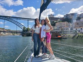 A group of friends poses on the deck of a sailboat, enjoying a scenic view of the city and bridge — a perfect moment for memorable boat trips.