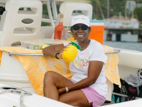 A joyful woman holds a pineapple drink on a boat, surrounded by refreshments and a vibrant atmosphere — perfect for a fun day on the water.