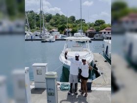 A cheerful couple waves from the dock next to their boat at the marina, ready for an exciting day on the water.