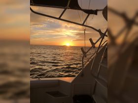 A stunning sunset view from the deck of a boat, showcasing the tranquil ocean and vibrant sky — perfect for evening cruises.