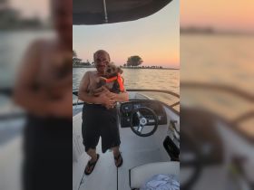 A man enjoys a beautiful sunset on a boat while holding his dog, showcasing a perfect moment of companionship on the water.