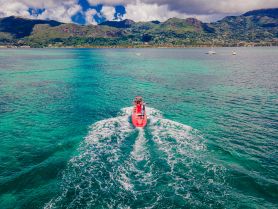 A vibrant red boat glides through crystal-clear waters, showcasing stunning island scenery in the background — perfect for adventure seekers exploring the coastline.