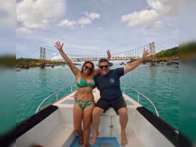 A joyful couple poses on a boat with arms raised, celebrating their adventure against the backdrop of a picturesque bridge — a perfect moment for memorable trips on the water.