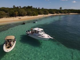 A vibrant scene at a beach with multiple boats anchored, showcasing a group enjoying the sun and water activities — perfect for a fun day out on the water.