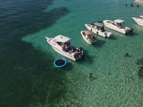 A lively scene at a sandbar with multiple boats anchored, where guests enjoy swimming and relaxing in the clear waters — perfect for a fun day on the water.