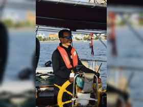 A cheerful captain navigates the boat, showcasing the joy of sailing on the open water.