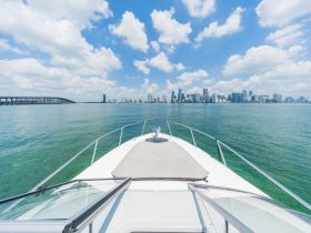 A stunning view from the front of a yacht cruising through clear waters, with the Miami skyline and a bridge in the background, showcasing the beauty of a day on the water.
