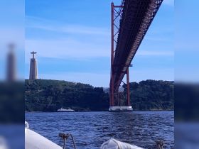 A picturesque view of a boat passing under a stunning bridge, with the iconic Christ the Redeemer statue in the background, showcasing the beauty of the landscape.