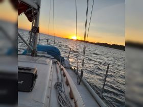 A serene sunset view from the deck of a sailboat, showcasing the tranquil waters and the beauty of the evening sky — perfect for a peaceful sailing experience.