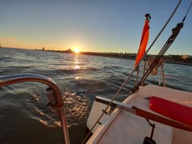 A serene sunset view from the deck of a sailboat, showcasing the tranquil waters and distant skyline — perfect for evening cruises.