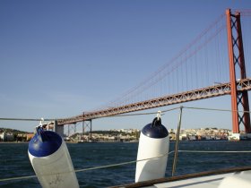 A scenic view of a boat with fenders in the foreground, showcasing the iconic bridge in the background — a perfect representation of maritime adventures in Lisbon.