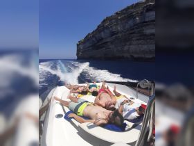 A group of friends relaxes and sunbathes on the deck of a boat, enjoying the stunning cliffside views and clear blue waters — a perfect summer getaway.
