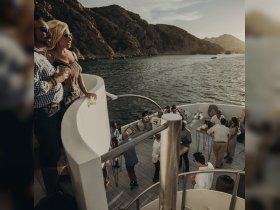 A couple enjoys drinks while overlooking the stunning coastline from the deck of a boat, capturing the essence of a lively boat party experience.