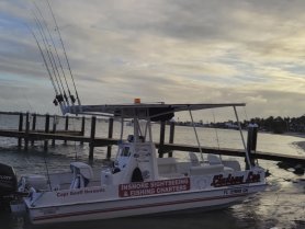 A sleek fishing boat, named 'Rodney Lee,' is docked by the waterfront, showcasing its fishing rods and inviting setup for charters.
