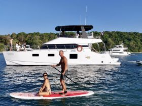 A couple enjoys paddleboarding in front of a luxurious yacht, capturing the essence of fun-filled water activities and relaxation on the water.