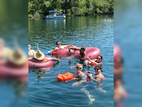 A lively group enjoys a fun day floating on pink tubes in the water, celebrating with drinks and laughter — the perfect summer getaway.
