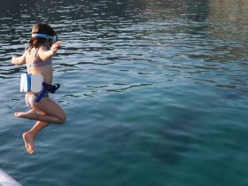 A child joyfully jumps into the clear waters, showcasing the excitement of summer fun and water activities — perfect for family adventures on the boat.