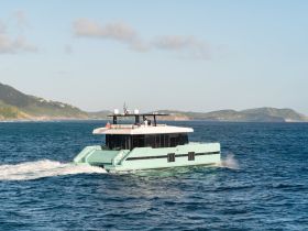 A sleek catamaran cruises through clear waters, showcasing its modern design against a scenic backdrop of hills — perfect for luxury charters and island hopping adventures.