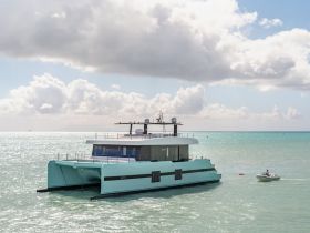 A stunning aerial view of a modern catamaran cruising through shimmering turquoise waters, showcasing its sleek design and luxurious features.