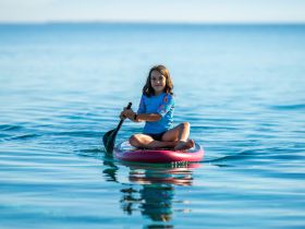 A young girl enjoys paddleboarding in calm waters, showcasing a fun and adventurous day on the water.