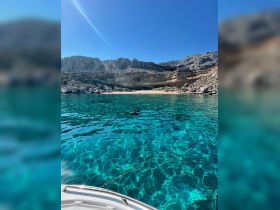 A stunning view of a secluded beach with crystal-clear waters and rocky cliffs, perfect for a relaxing day on the boat or exploring the coastline.
