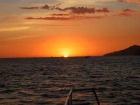 A stunning sunset over the ocean, with silhouettes of boats and a distant coastline, creating a picturesque backdrop for evening cruises.