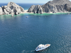 A stunning aerial view of a yacht cruising near rocky cliffs and a secluded beach, showcasing the beauty of the coastline and clear blue waters.