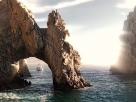 A stunning view of a boat passing through a natural rock arch, showcasing the breathtaking coastline and scenic beauty of the area.