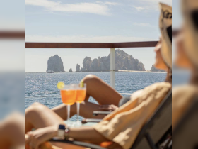 A guest enjoys refreshing cocktails while relaxing on a boat, with stunning rock formations in the background — a perfect setting for a luxurious day at sea.