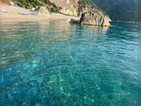 A serene view of clear waters with a rocky shoreline, ideal for capturing the beauty of coastal landscapes.