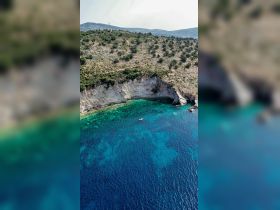 A stunning aerial view of a secluded coastline with crystal-clear waters, showcasing a small boat anchored in a picturesque bay — perfect for exploring hidden gems while boating.