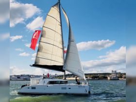 A stunning catamaran named 'Desta Vez' sails gracefully on the water, showcasing its vibrant sails against a picturesque backdrop.