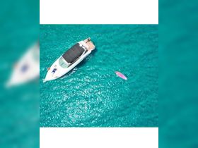 An aerial view captures a vibrant scene of a boat anchored in crystal-clear waters, with a person paddleboarding nearby — a perfect snapshot of summer fun on the water.