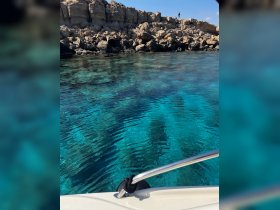 A stunning view of crystal-clear waters and rocky coastline, with a person standing on the rocks, showcasing the beauty of the destination.